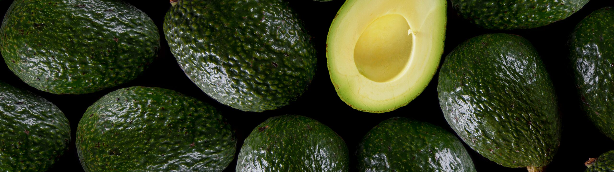 A close mass of avocados seen from directly above, with one cut in half among them.